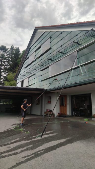 Ein Mann reinigt eine Glasfassade eines modernen Gebäudes mit einem Hochdruckreiniger.